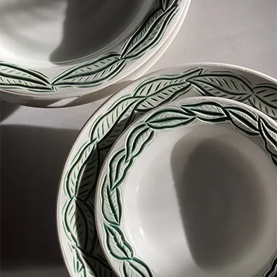 a set of white plates with leaves carved around their edges, with green glaze in the carved areas